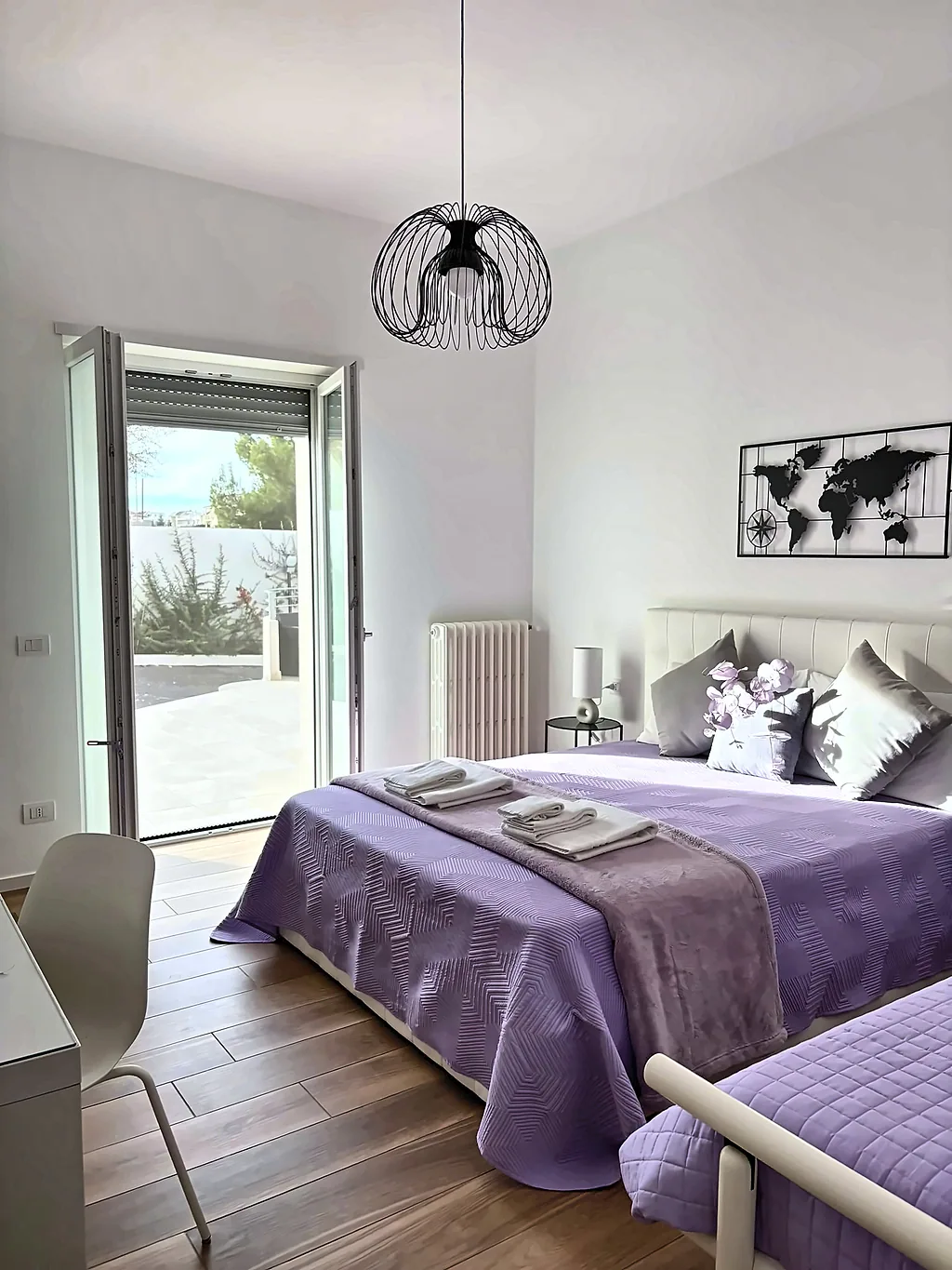 La camera Betulla vista dall'ingresso: letto matrimoniale con copriletto lilla, letto singolo e portafinestra