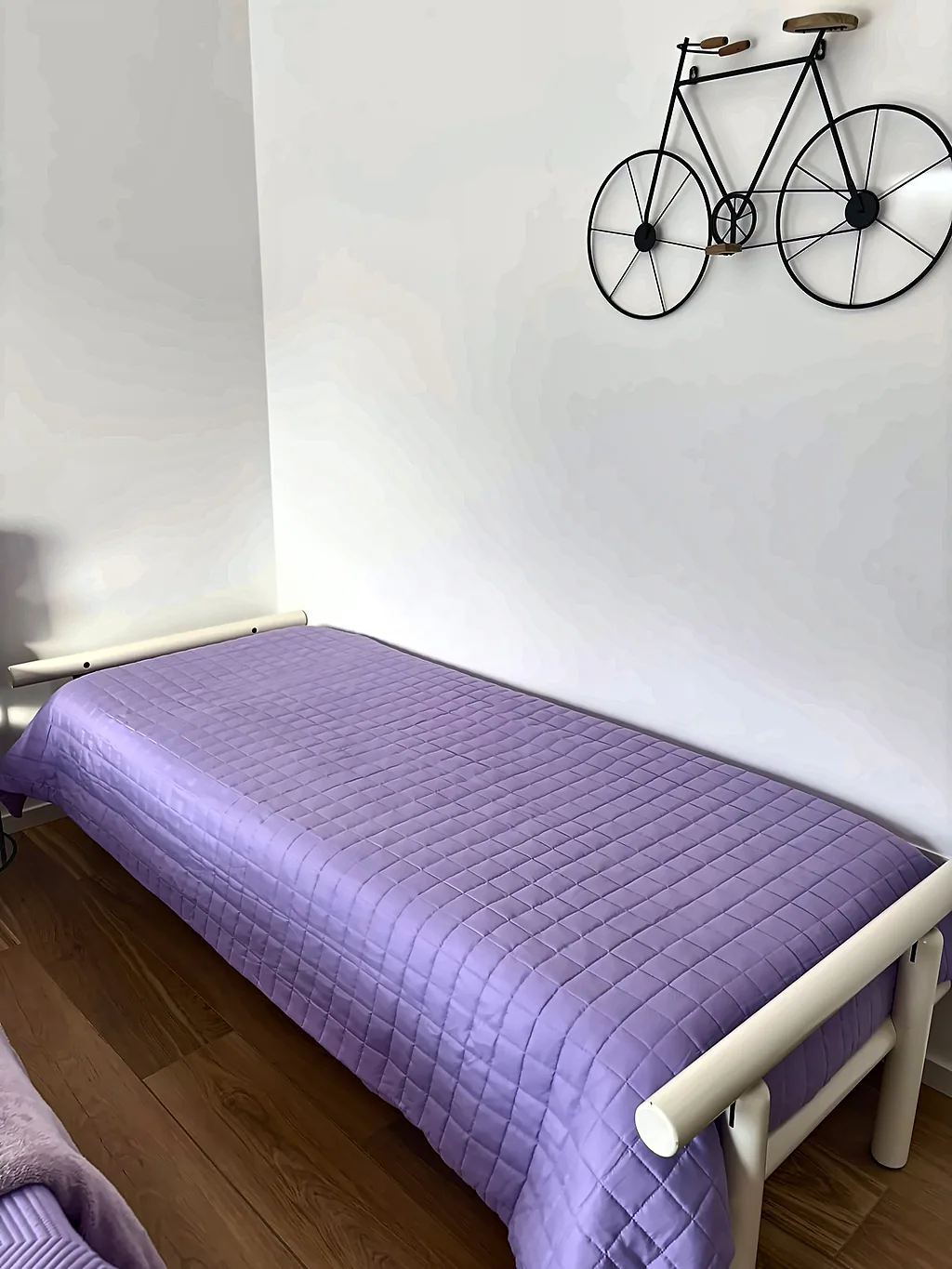Il letto singolo con copriletto lilla e una bicicletta decorativa appesa alla parete