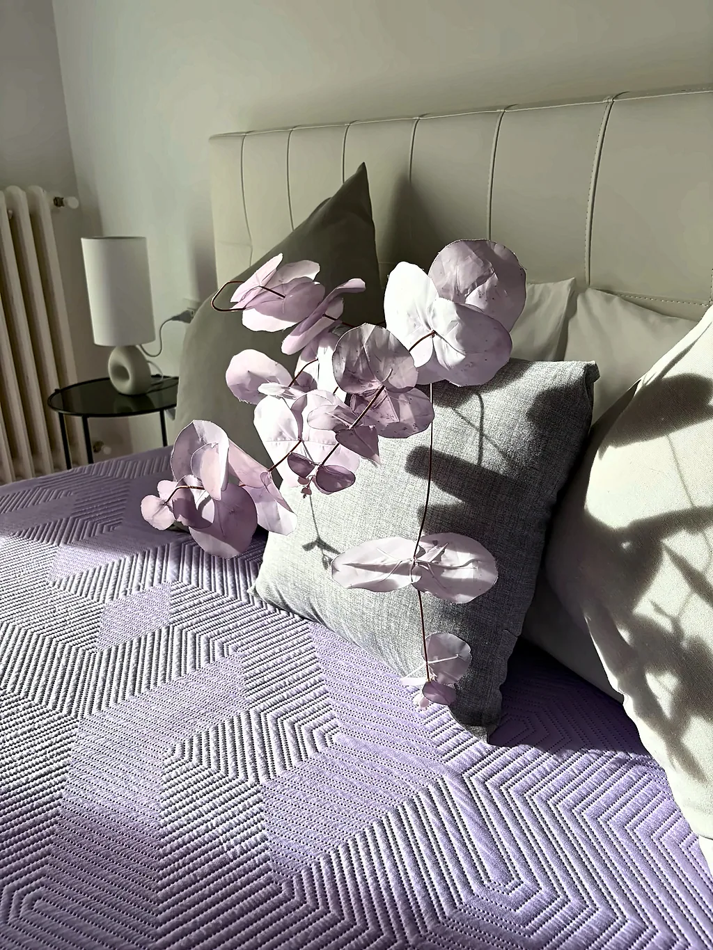 Dettaglio dei cuscini con un ramo di fiori lilla sul letto