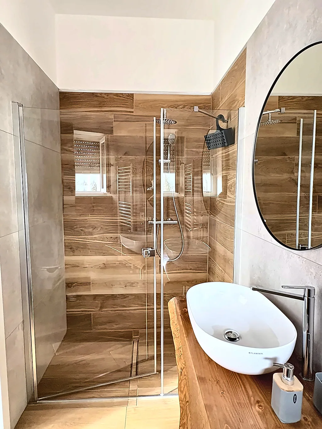 La doccia a filo pavimento con parete effetto legno e il lavabo in primo piano