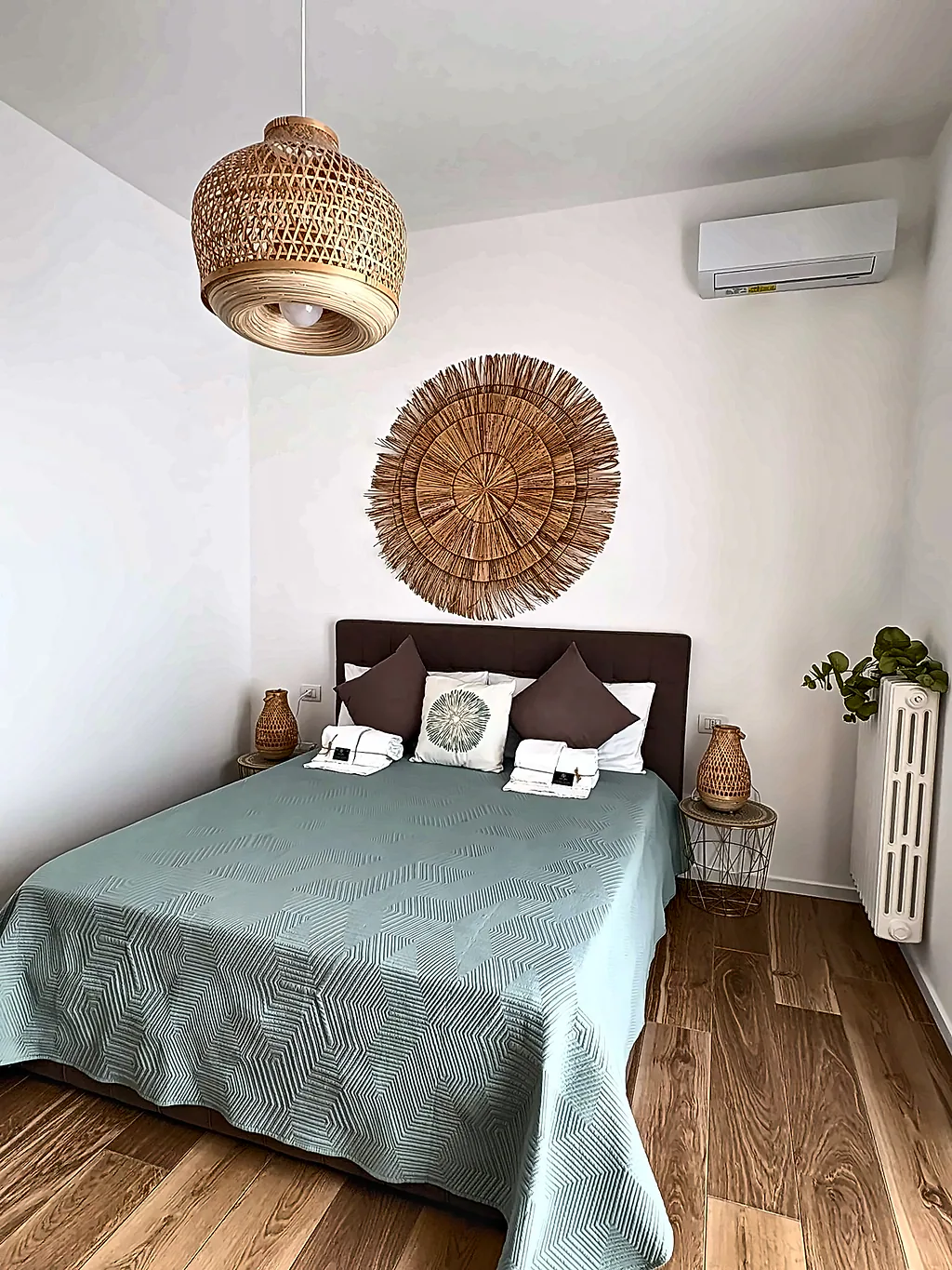 Il letto matrimoniale della camera Ginkgo, con copriletto verde salvia, decorazione rotonda in paglia e lampada in rattan