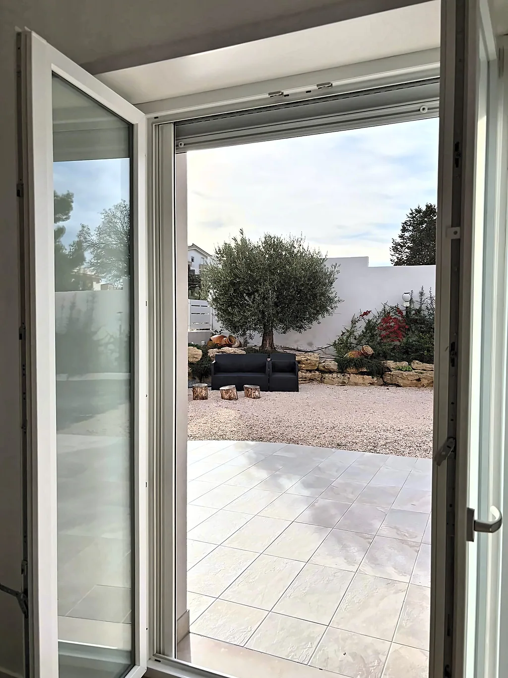 La portafinestra aperta sul patio, con vista sull'ulivo e sull'area relax del giardino