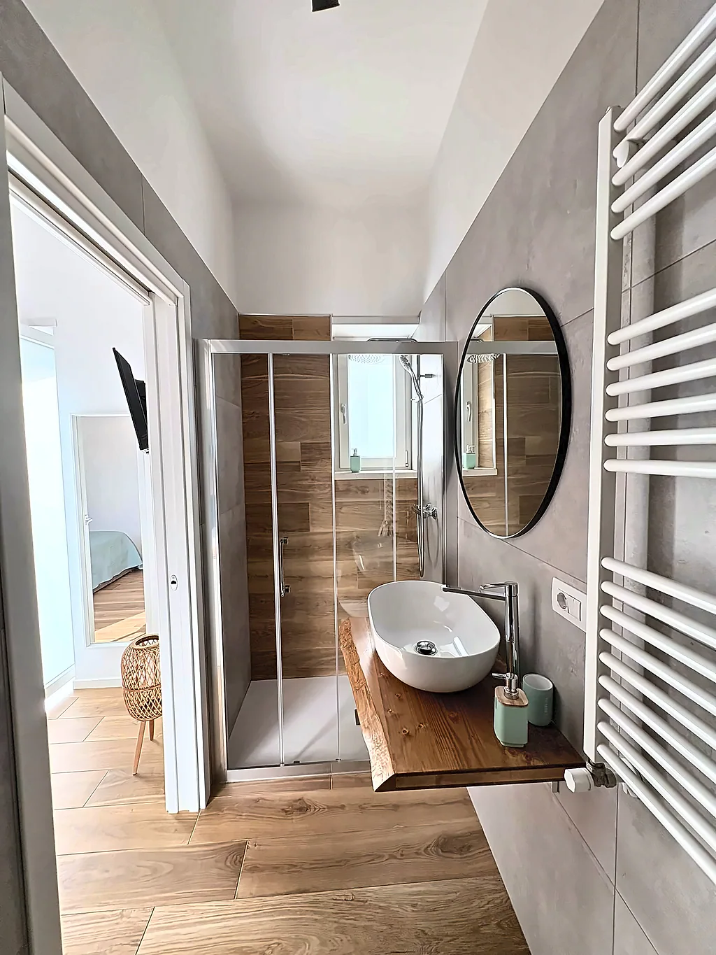 Il bagno visto dalla camera, con il lavabo, lo specchio rotondo e la doccia sullo sfondo