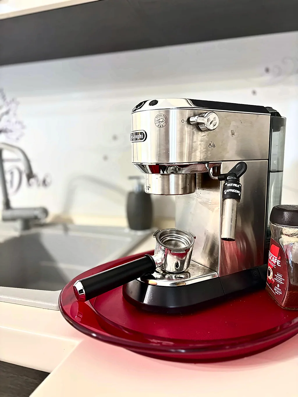 Una macchina per il caffè espresso in acciaio su un vassoio rosso, accanto al lavello