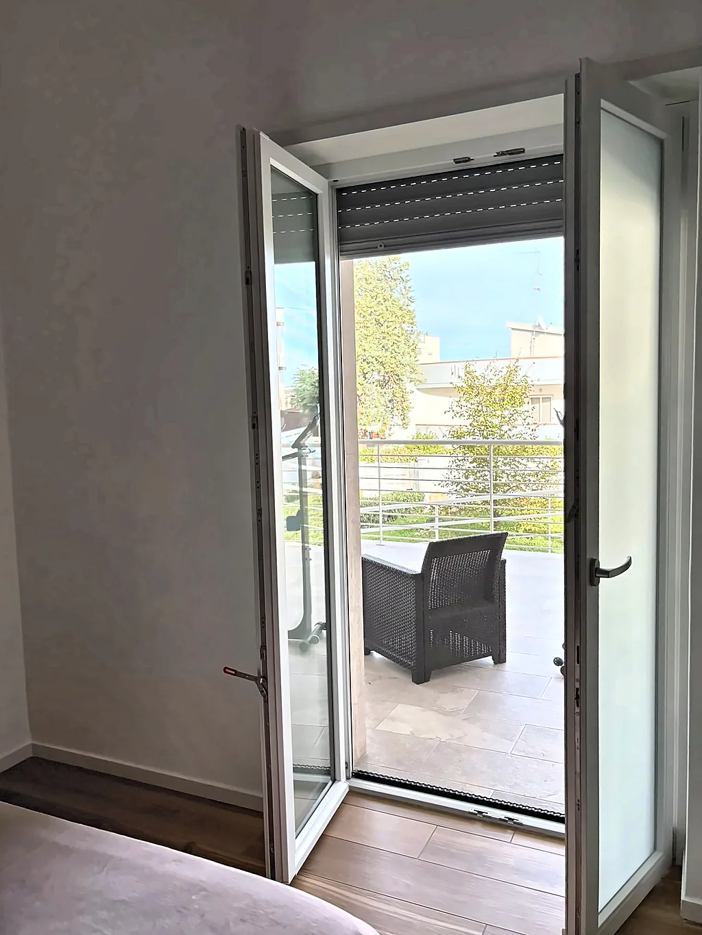 La portafinestra aperta sul balcone, con una poltrona da esterno e vista sul giardino